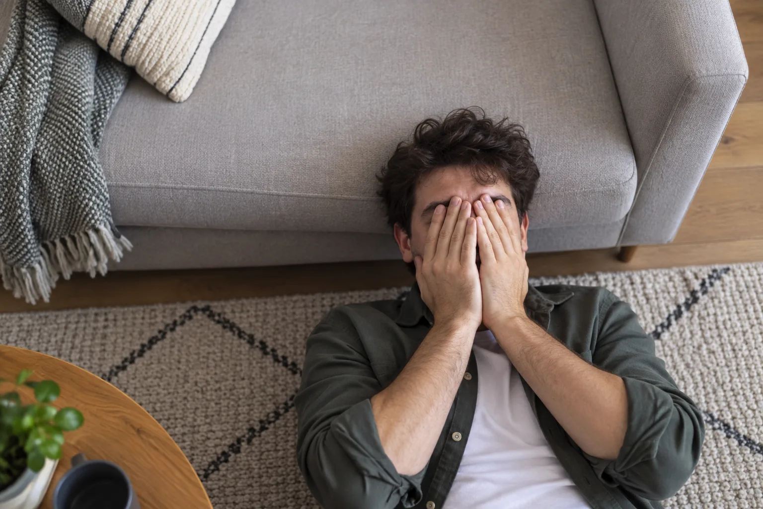 Man lying on the floor at home covering his face while experiencing migraine symptoms