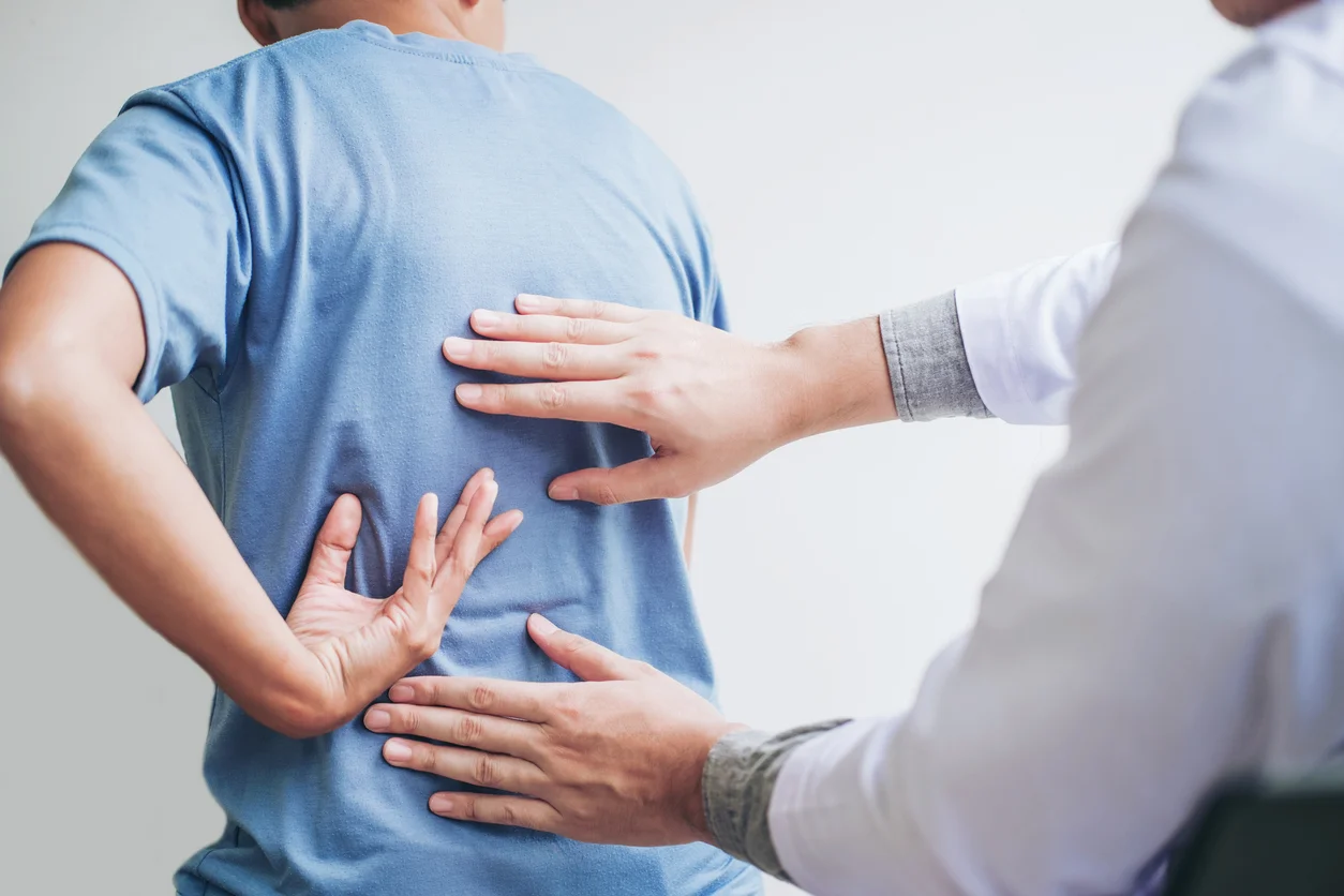 Specialist examining a patient with back pain during a clinical evaluation, focusing on the lower back area