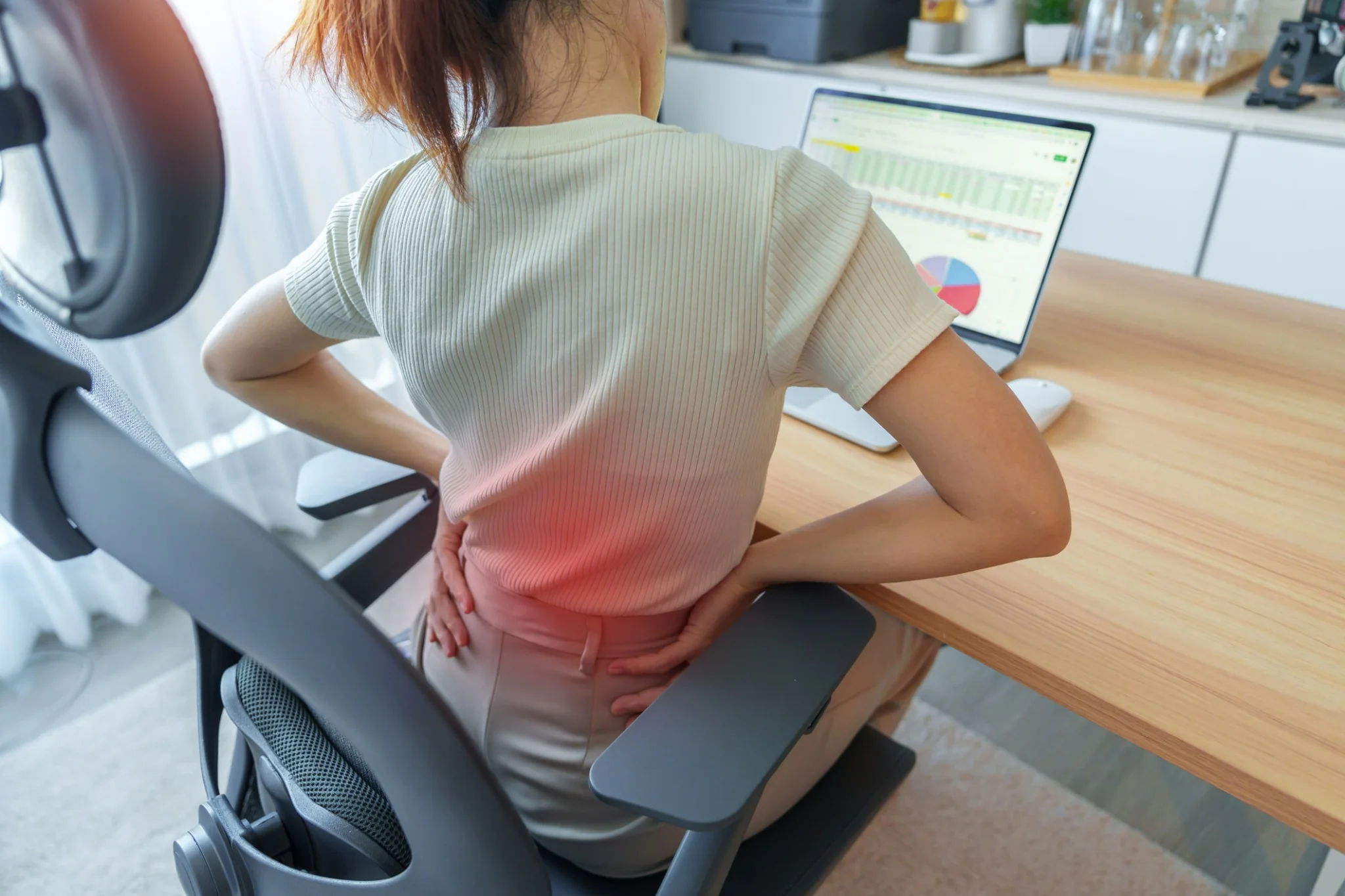 Woman experiencing lower back pain while sitting and working at a desk