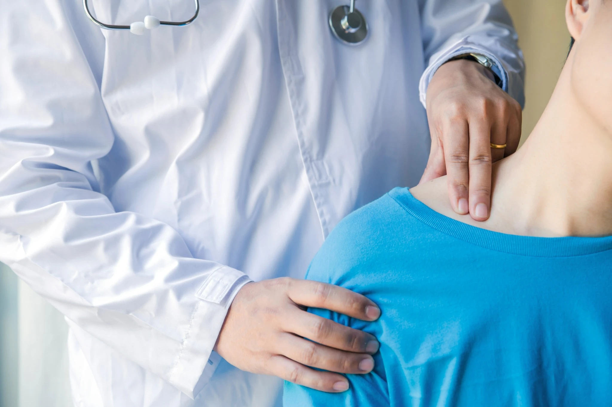 Doctor examining a patient’s neck and upper back during a medical consultation