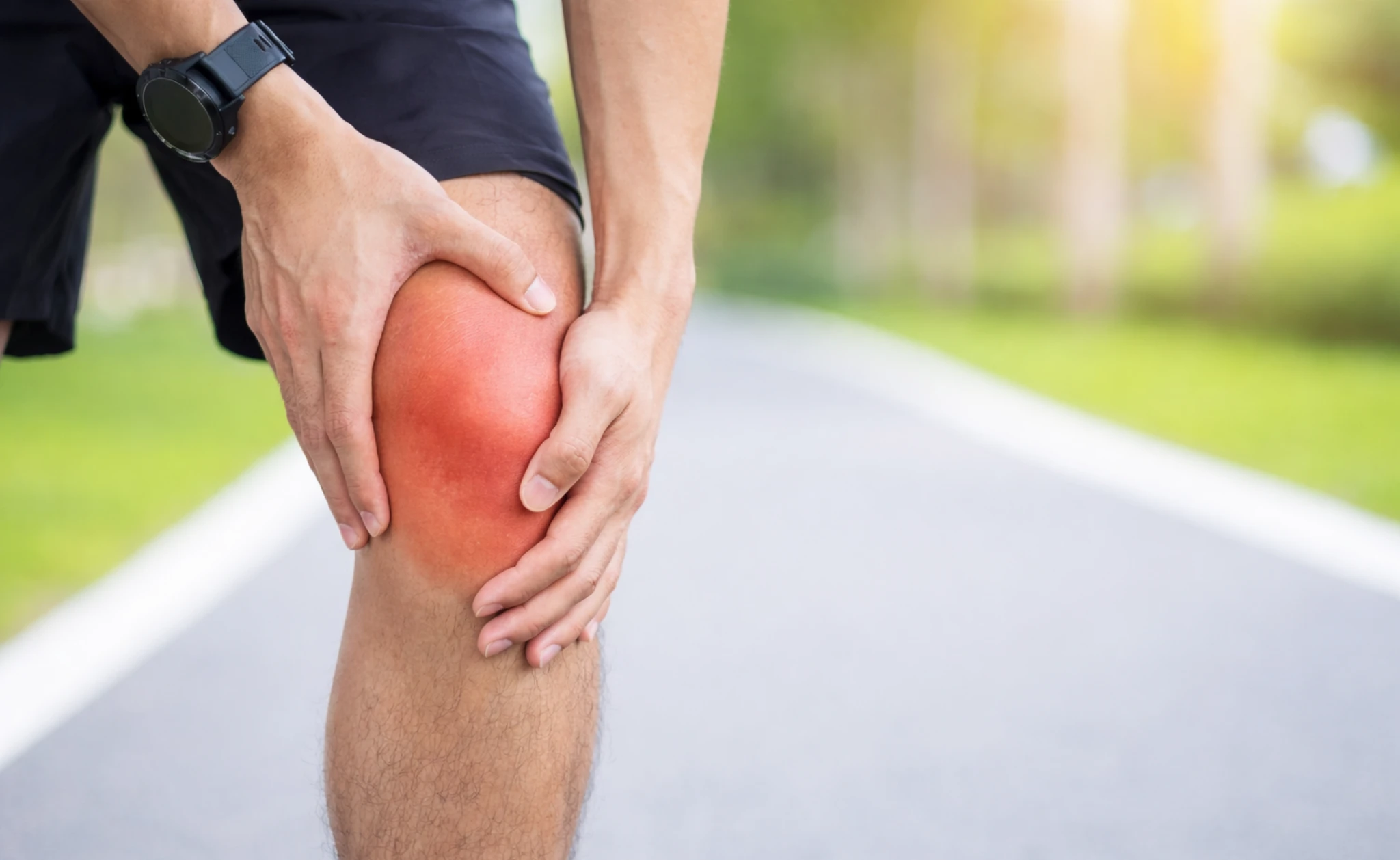 Close-up of a person holding a painful knee outdoors, representing leg pain after exercise or running.