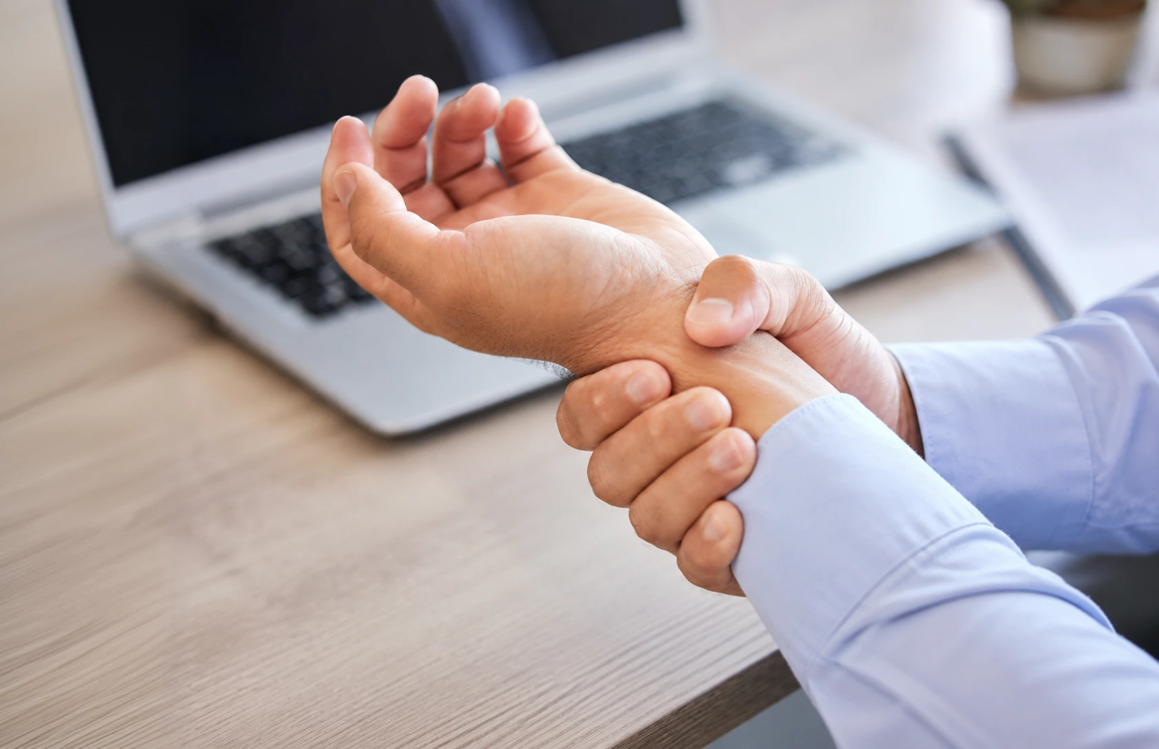 Person holding their wrist near a laptop, representing hand numbness, tingling, or wrist discomfort.