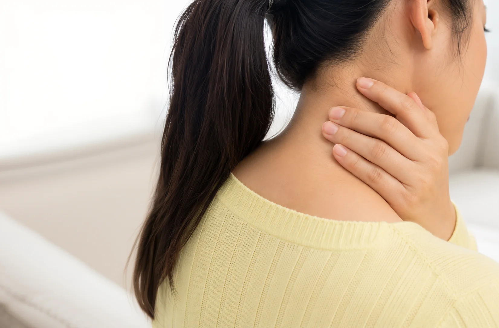 Woman holding the back of her neck while experiencing neck pain and stiffness.