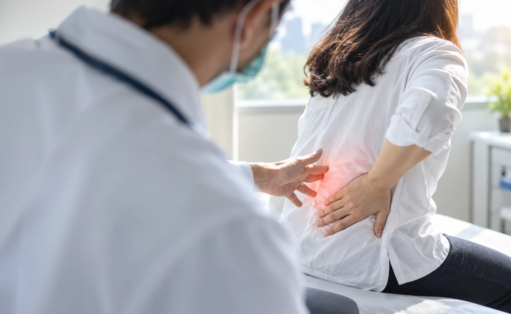 Doctor evaluating a patient’s lower back pain during a medical visit in an exam room.